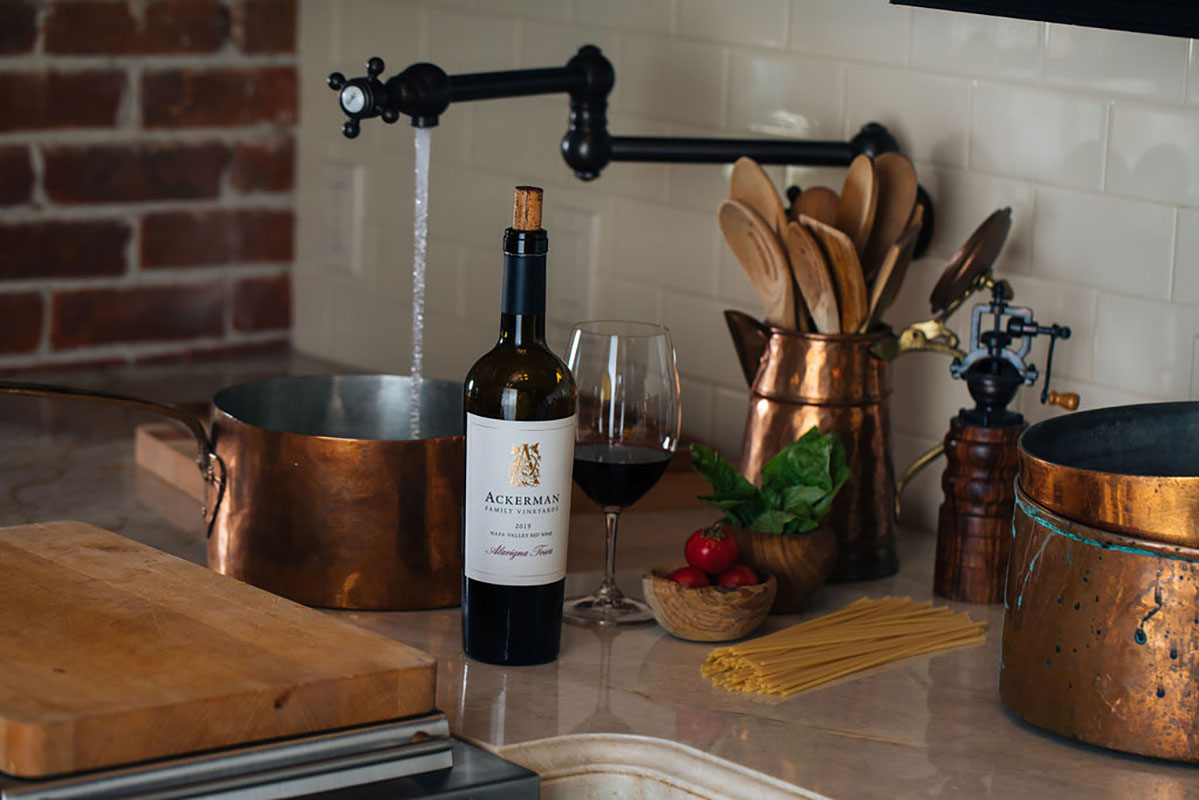 bottle of Ackerman Family Vineyards wine on a kitchen counter surrounded by cooking utensils